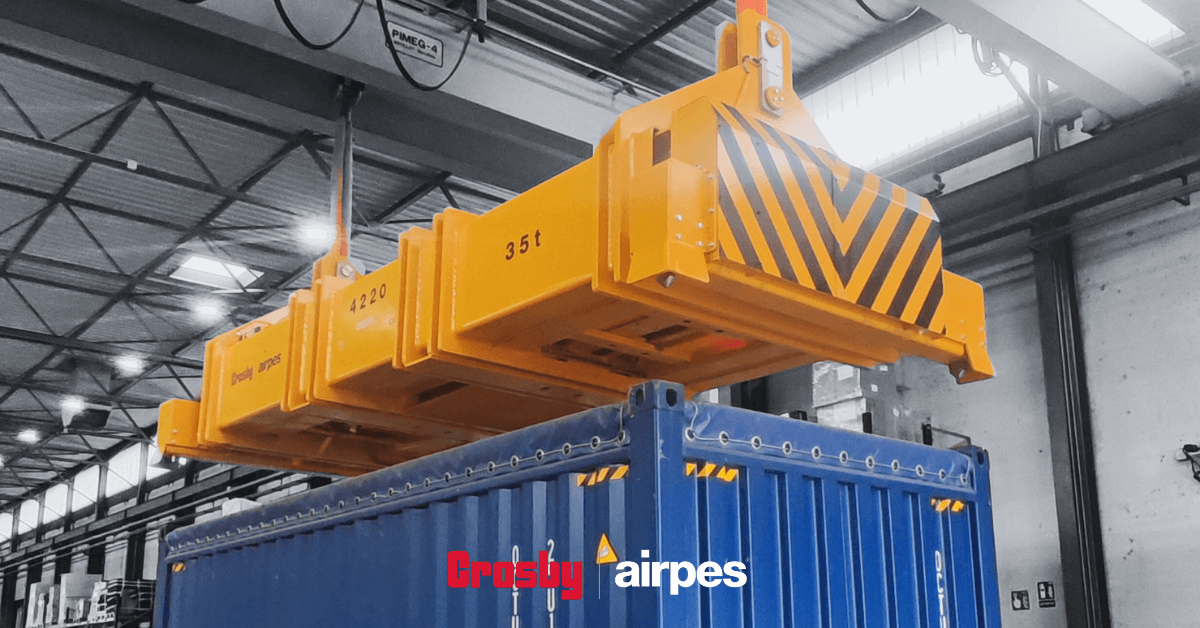 Hydraulic lifting spreader beam by Crosby Airpes lifting a 40-foot container with twist lock system and status lights in port environment.