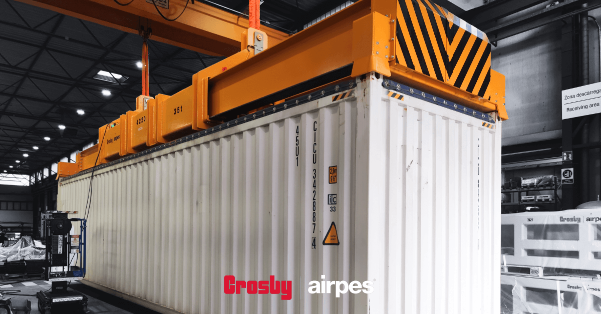 Hydraulic lifting spreader beam by Crosby Airpes lifting a 40-foot container with twist lock system and status lights in port environment.