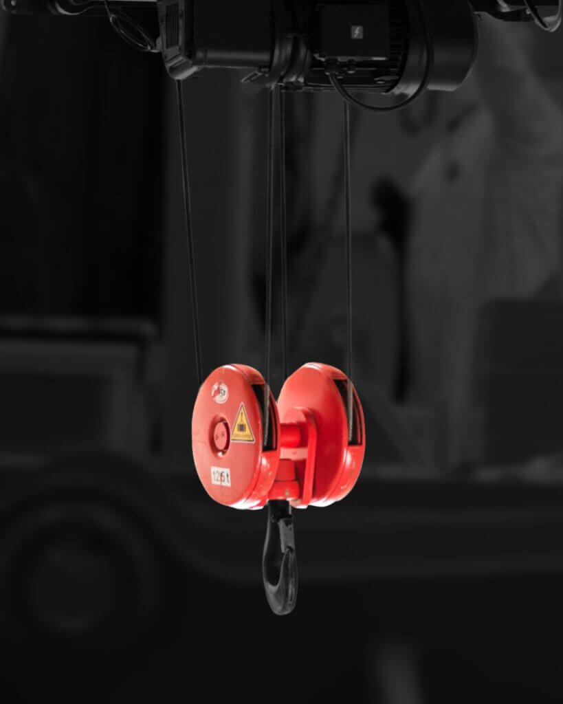 Red crane hook block suspended from overhead hoist for lifting operations